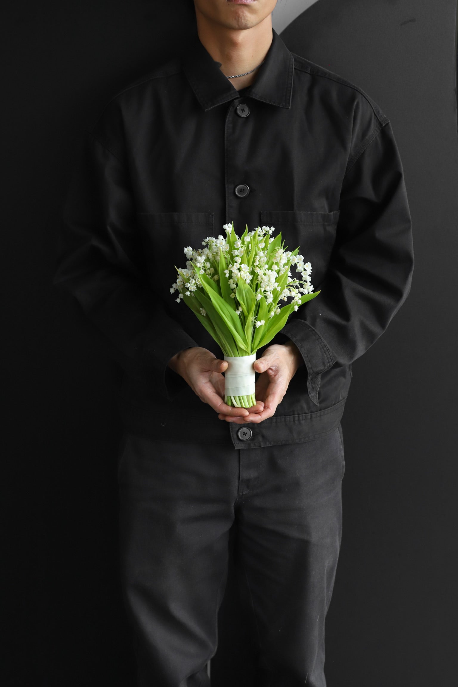 Compact all-Lily of the Valley bridal bouquet with white bell-shaped blooms and deep green leaves, stem wrapped in white satin ribbon, photographed against a dark background — Just Bloom Hong Kong