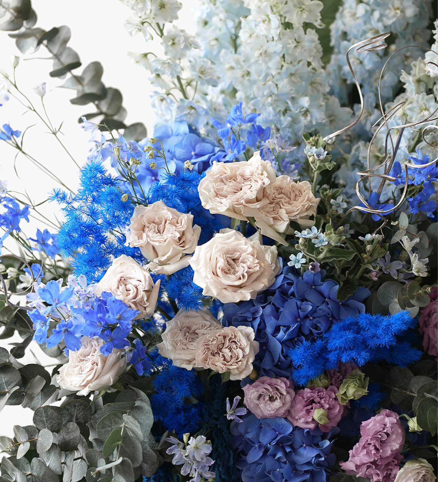 Raegan close-up featuring blush roses, blue delphiniums, purple carnations, and vivid blue accents