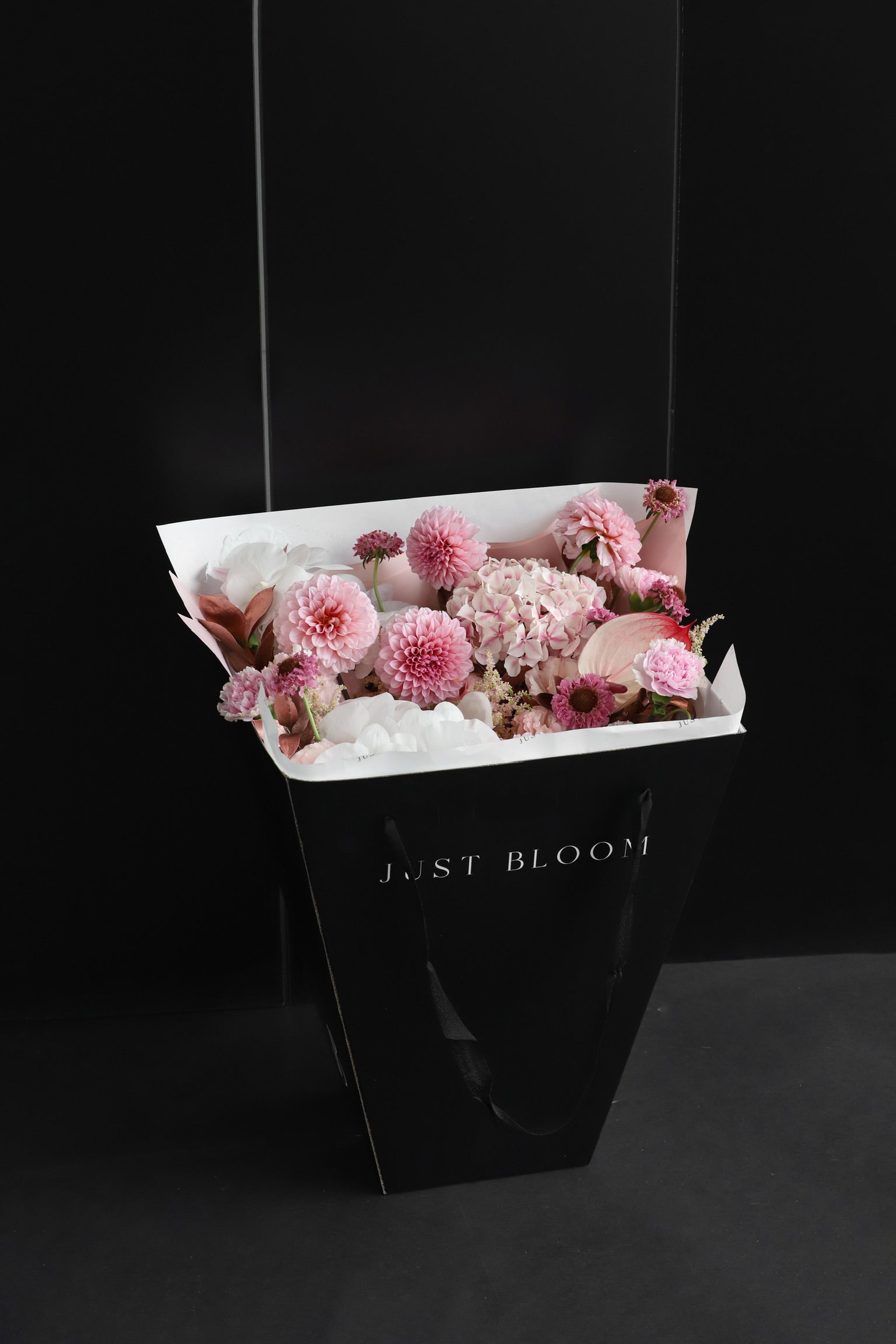 Just Bloom signature black gift bag carrying a large soft pink and white fresh flower bouquet with spherical and layered blooms against a dark background — Just Bloom Hong Kong
