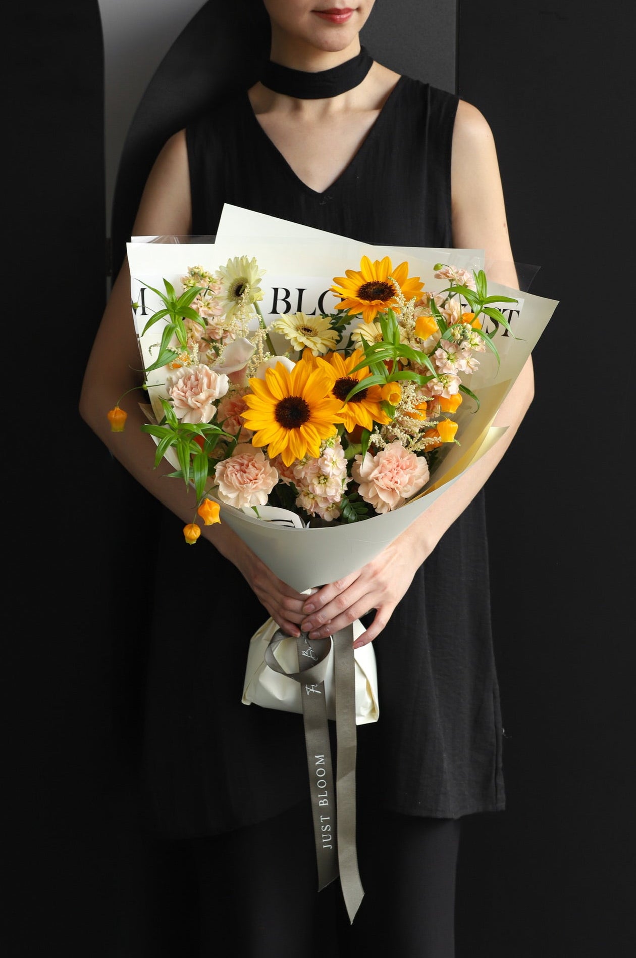 Model holding a warm fresh flower bouquet with sunflowers and blush seasonal blooms wrapped in white Just Bloom paper with grey ribbon — Just Bloom Hong Kong
