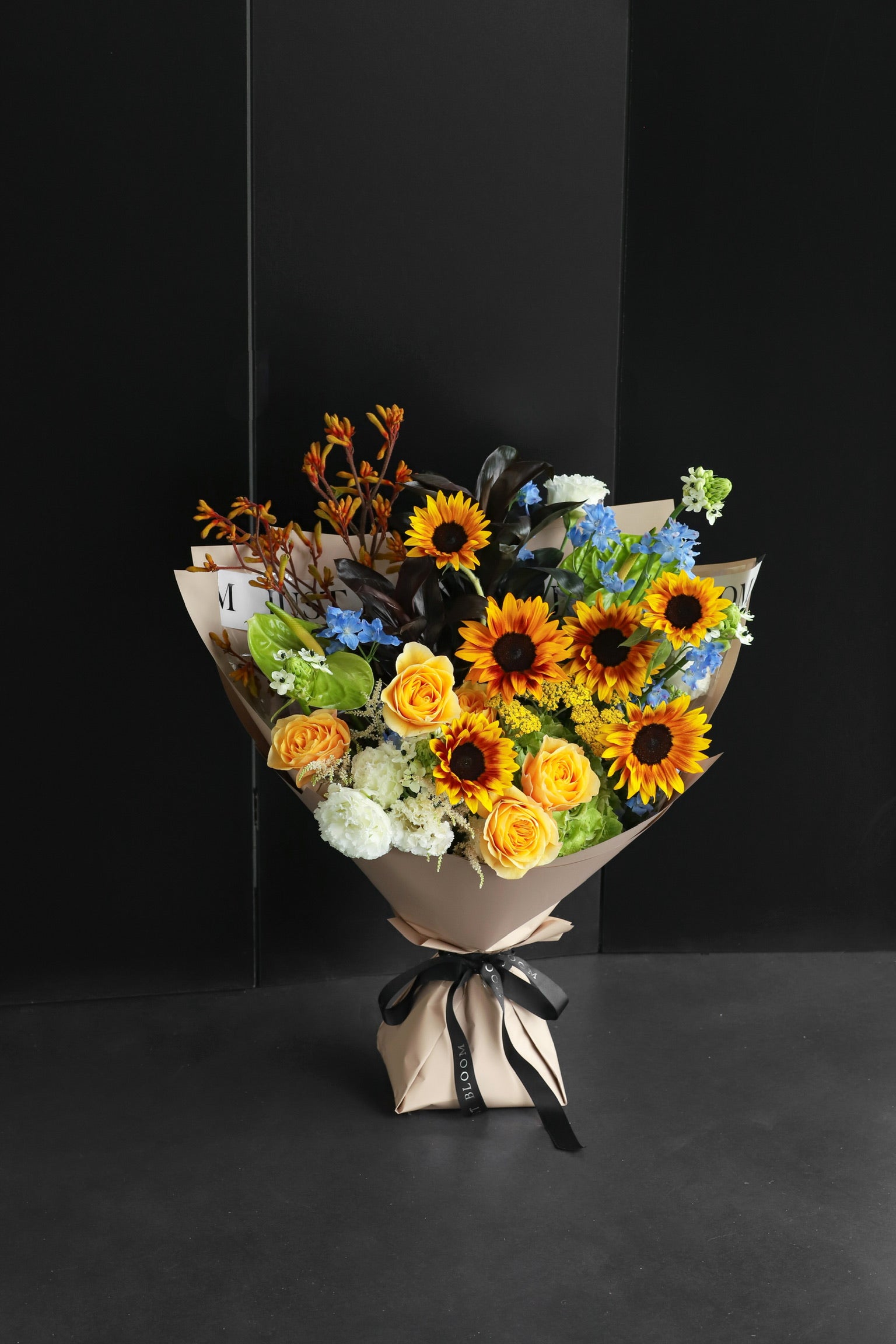 Bold sun-toned fresh flower bouquet featuring Japanese sunflowers, roses, and mixed seasonal blooms, wrapped in kraft paper with black ribbon — Just Bloom Hong Kong