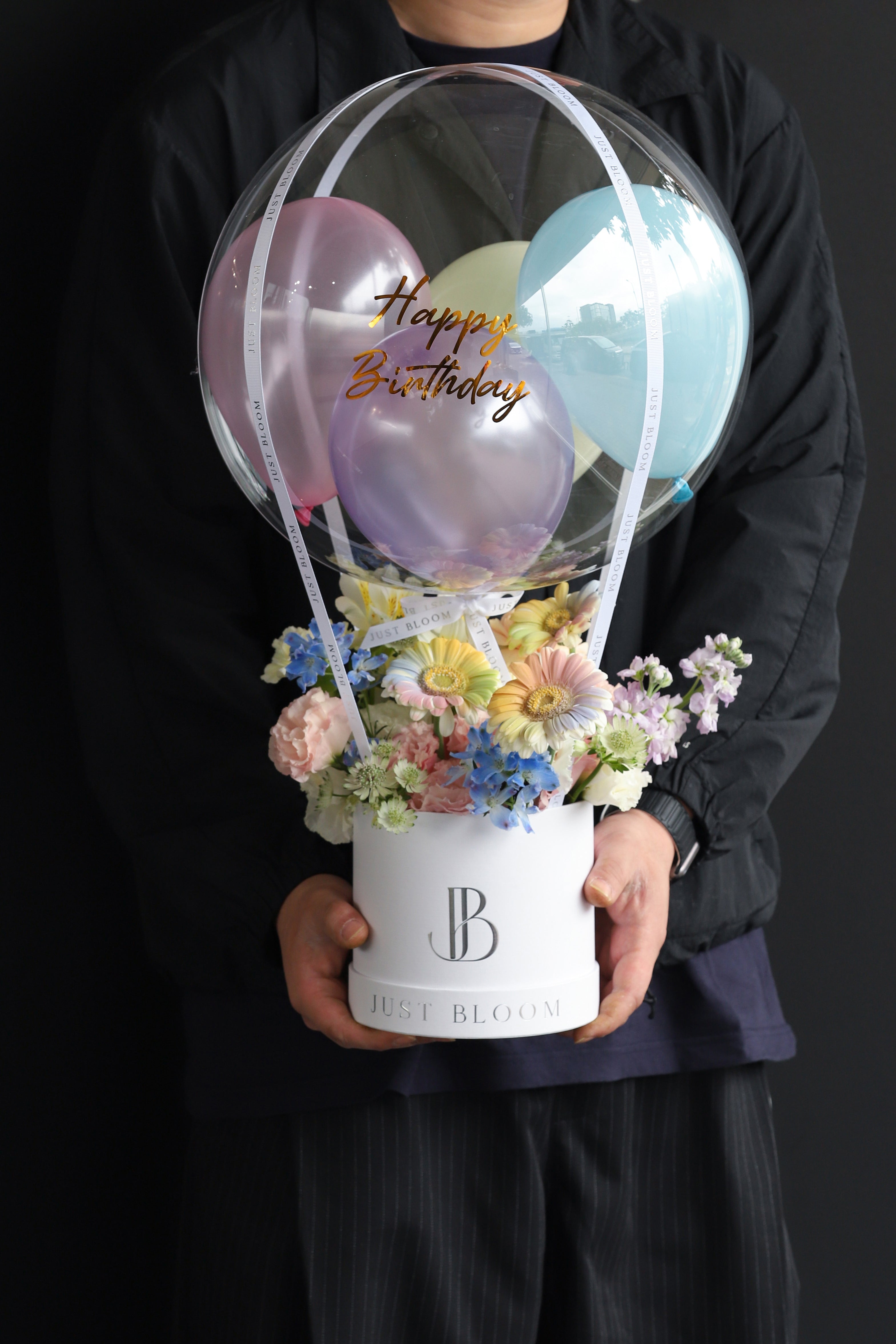 Model holding a playful pastel fresh flower box with mixed Gerberas, Stocks, and Delphiniums in a white Just Bloom round box against a dark background — Just Bloom Hong Kong