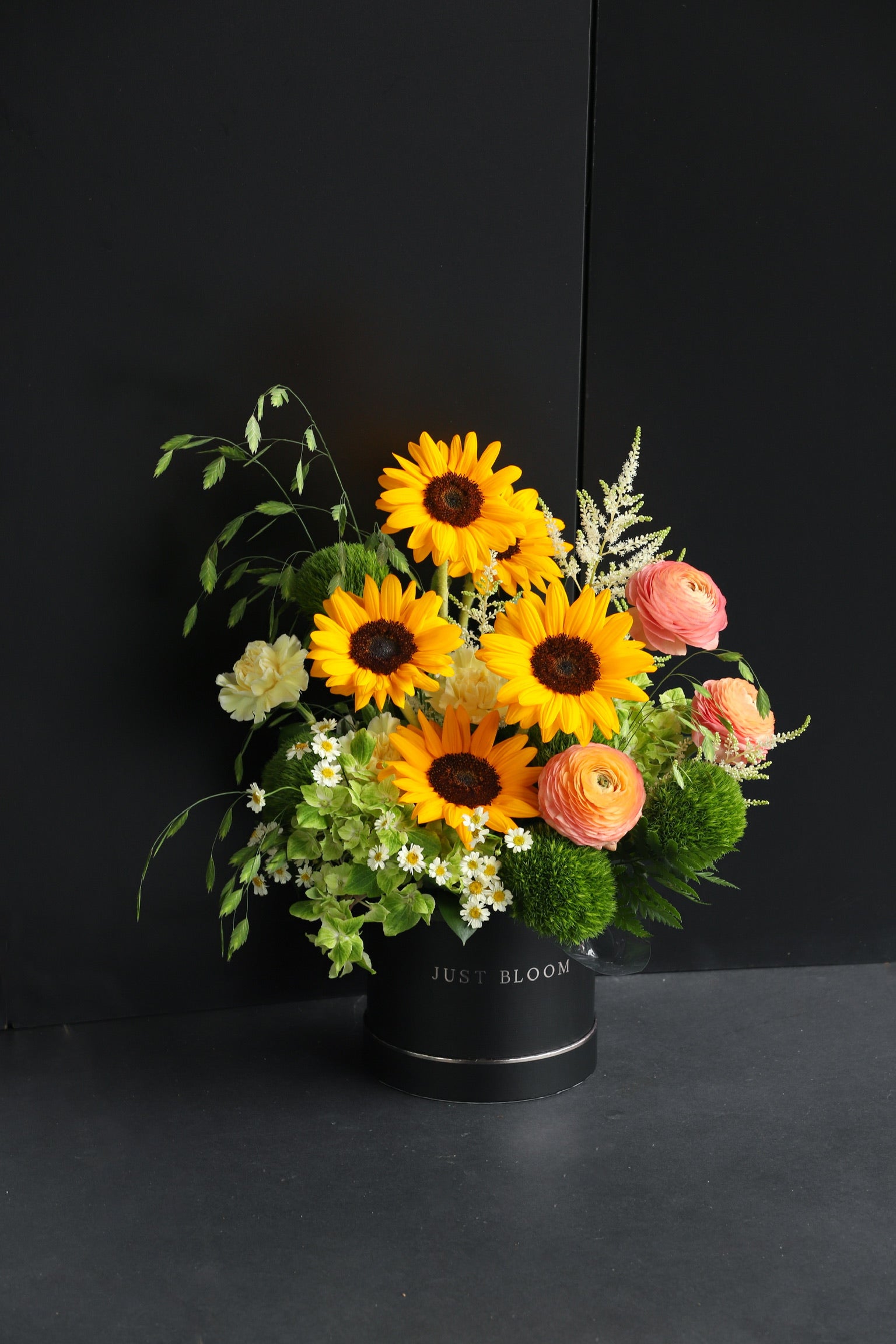 Warm-toned fresh flower box arrangement with sunflowers and mixed peach and cream seasonal blooms in a black Just Bloom hat box against a dark background — Just Bloom Hong Kong