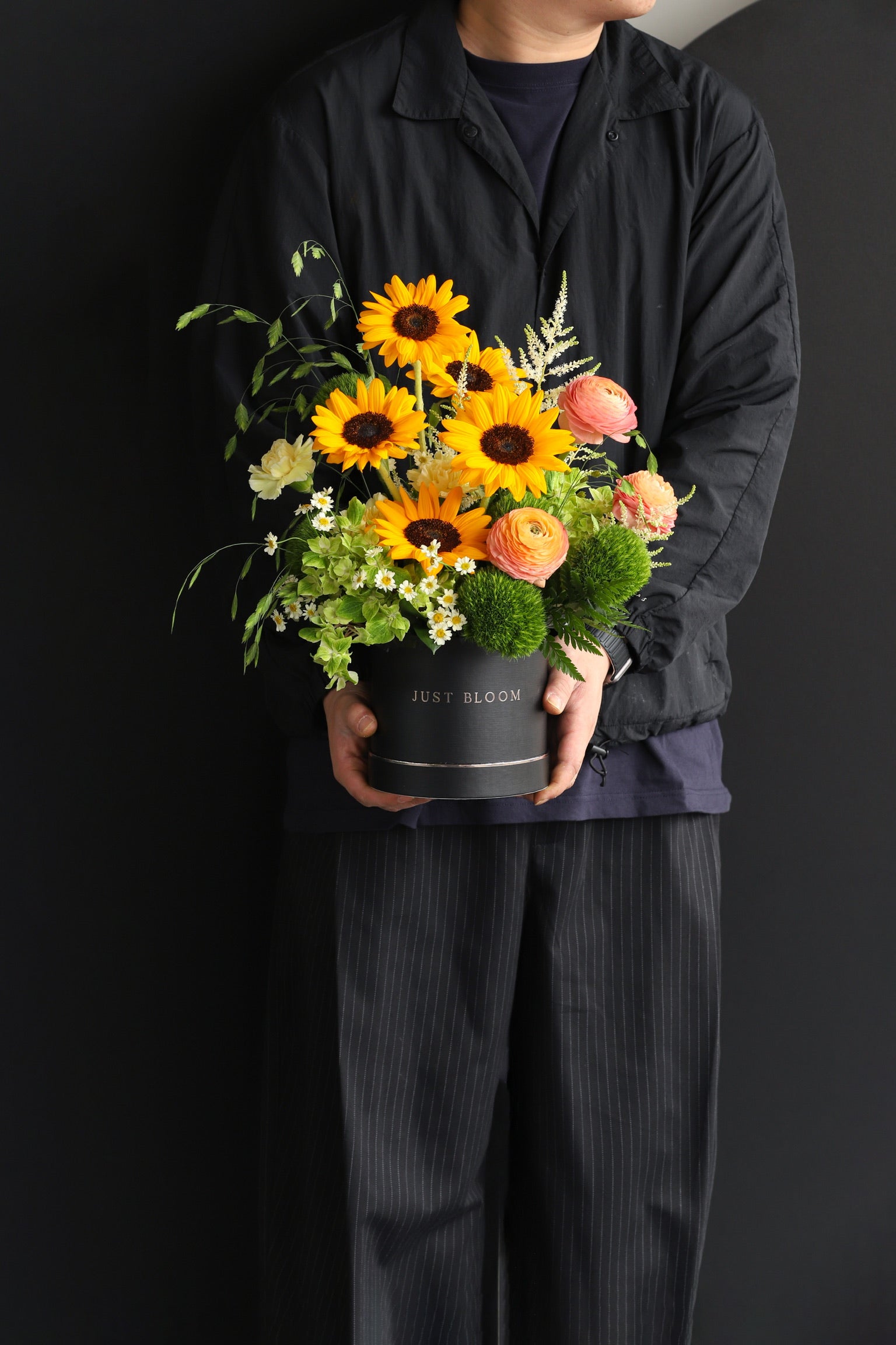 Model holding a warm-toned flower box arrangement with sunflowers, ranunculus, and mixed seasonal blooms in a black Just Bloom hat box — Just Bloom Hong Kong