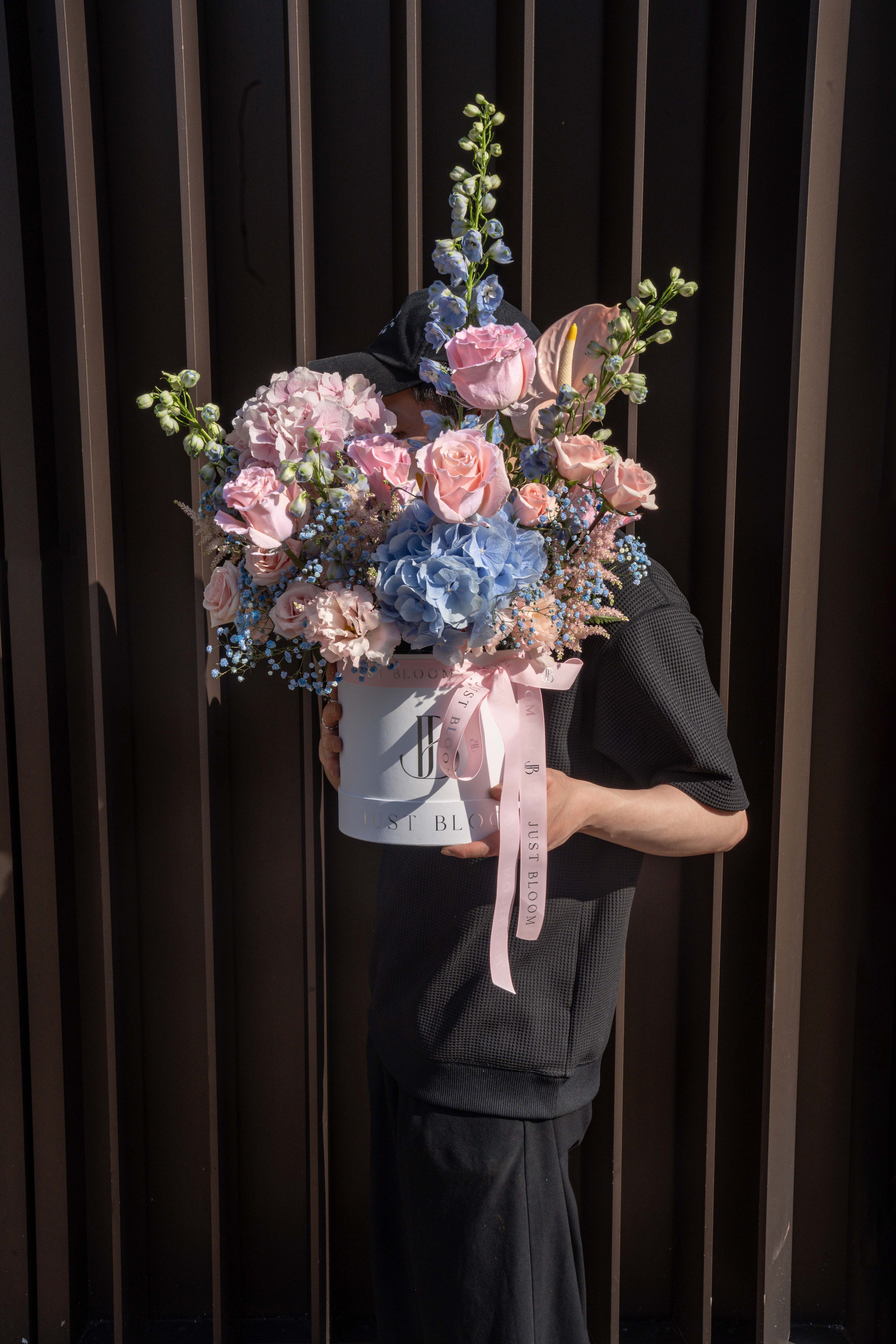 Person holding the Sweet Rhapsody flower box outdoors against a slatted wall backdrop — Just Bloom Hong Kong