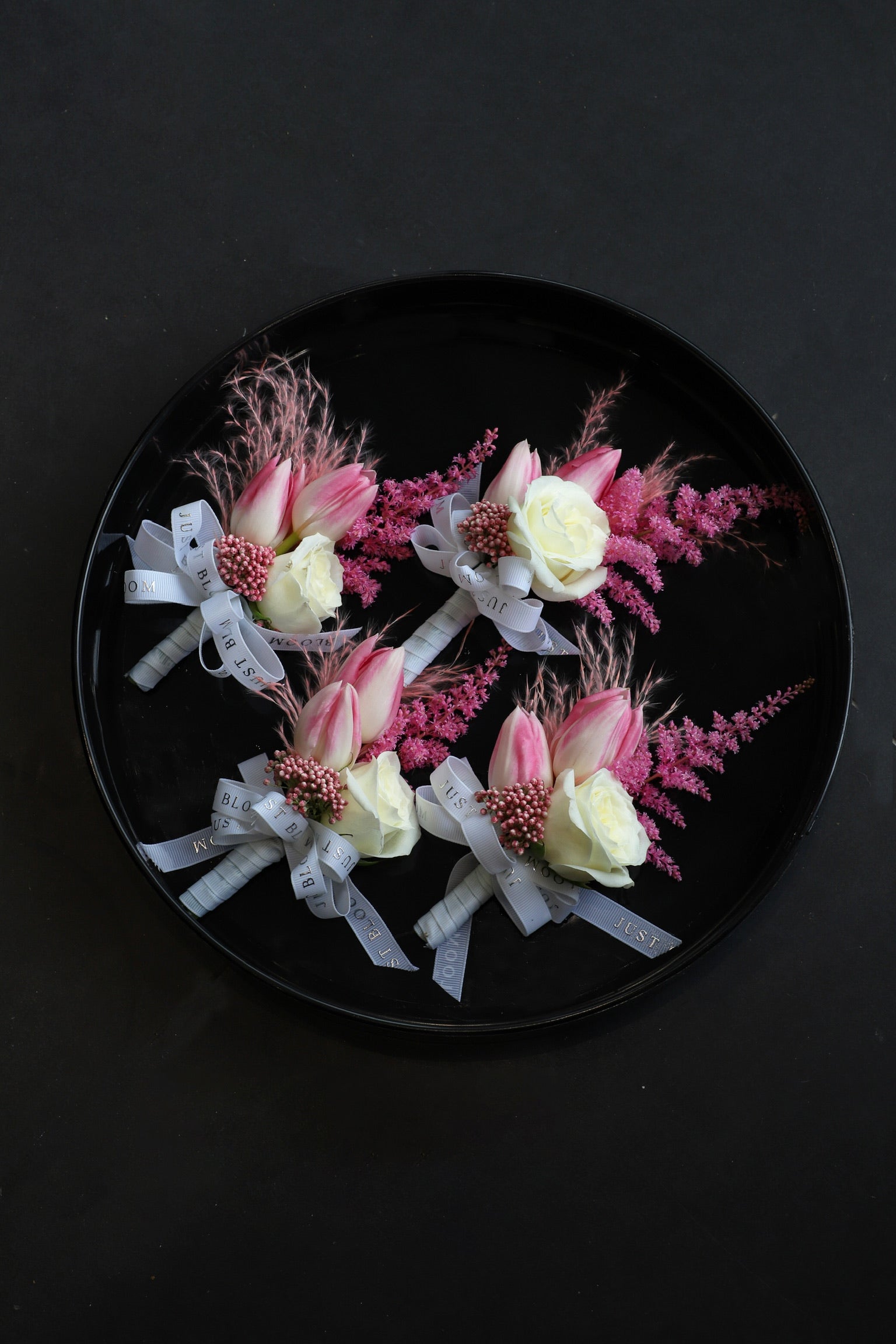 Four Sweet Vow corsages arranged on a black tray featuring pink tulips, white spray roses, deep pink astilbes and rice flowers tied with Just Bloom grey ribbon — Just Bloom Hong Kong