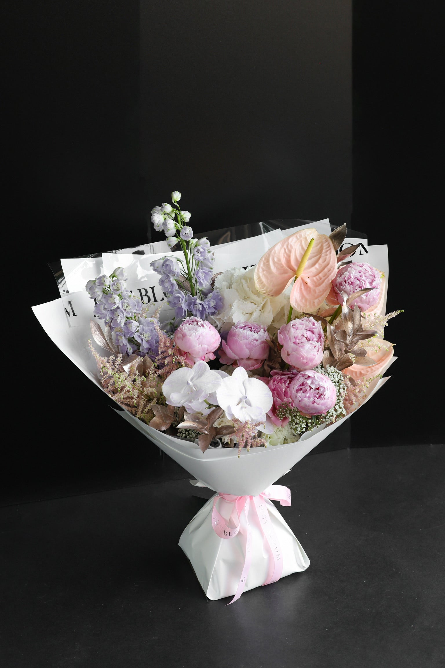 The Dreamer luxury bouquet by Just Bloom Hong Kong featuring pink peonies, lavender delphiniums, white orchids, astilbes and anthuriums in white wrapping with Just Bloom pink ribbon