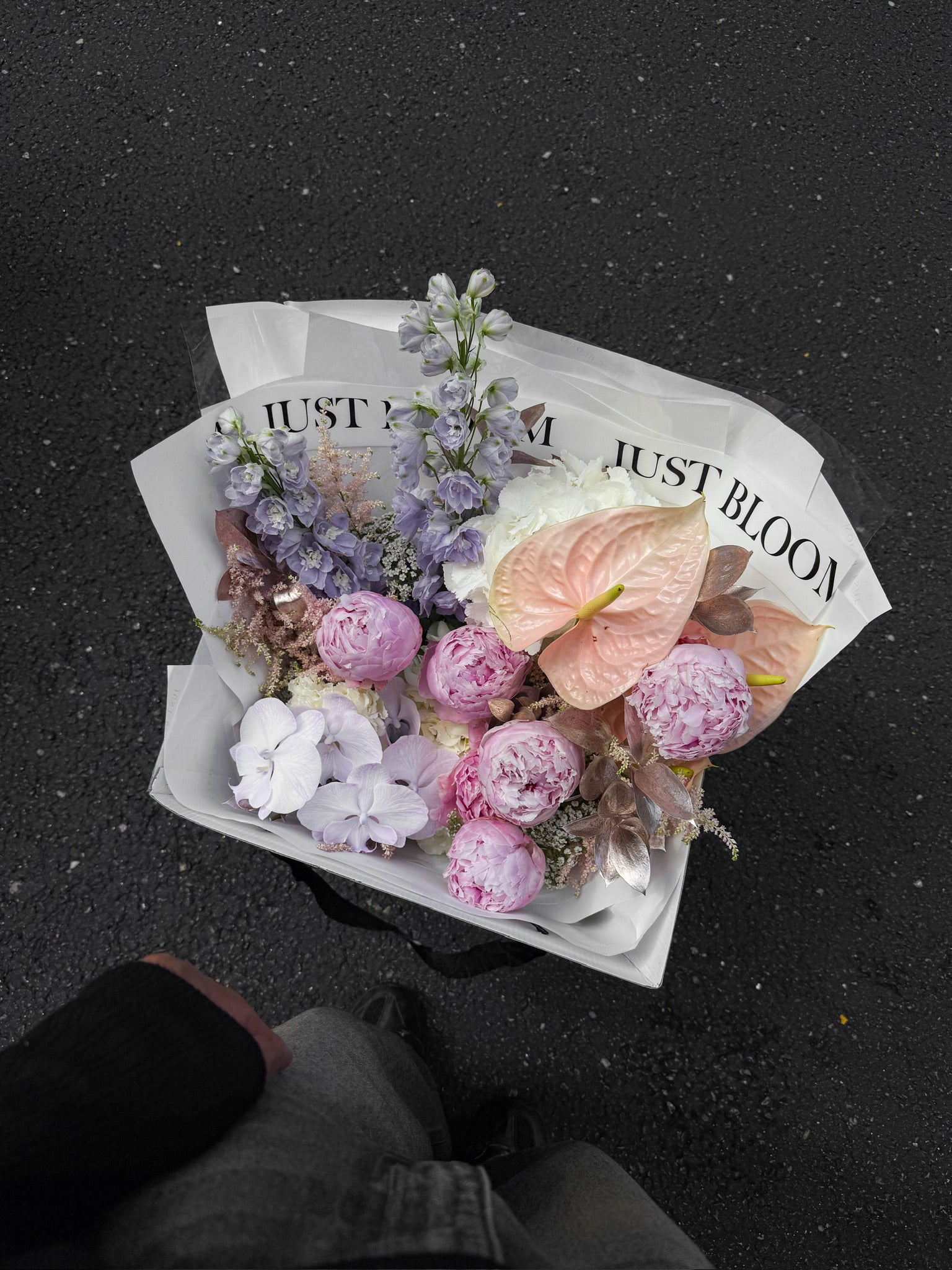 The Dreamer luxury bouquet by Just Bloom Hong Kong photographed from above, showcasing pink peonies, lavender delphiniums, phalaenopsis orchids and anthuriums in white Just Bloom wrapping