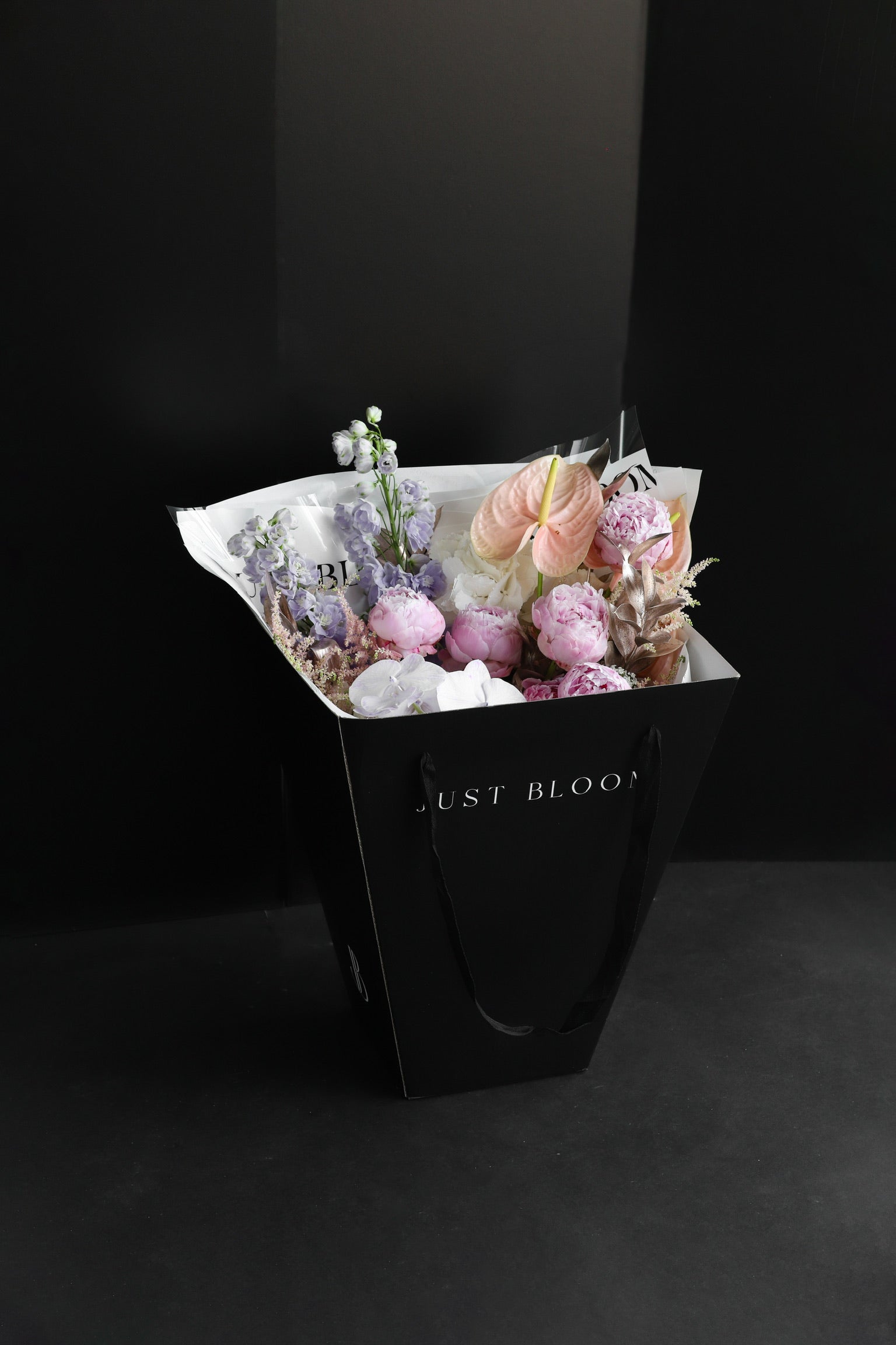 The Dreamer luxury bouquet by Just Bloom Hong Kong presented in a black Just Bloom tote bag, showcasing pink peonies, lavender delphiniums, orchids and anthuriums