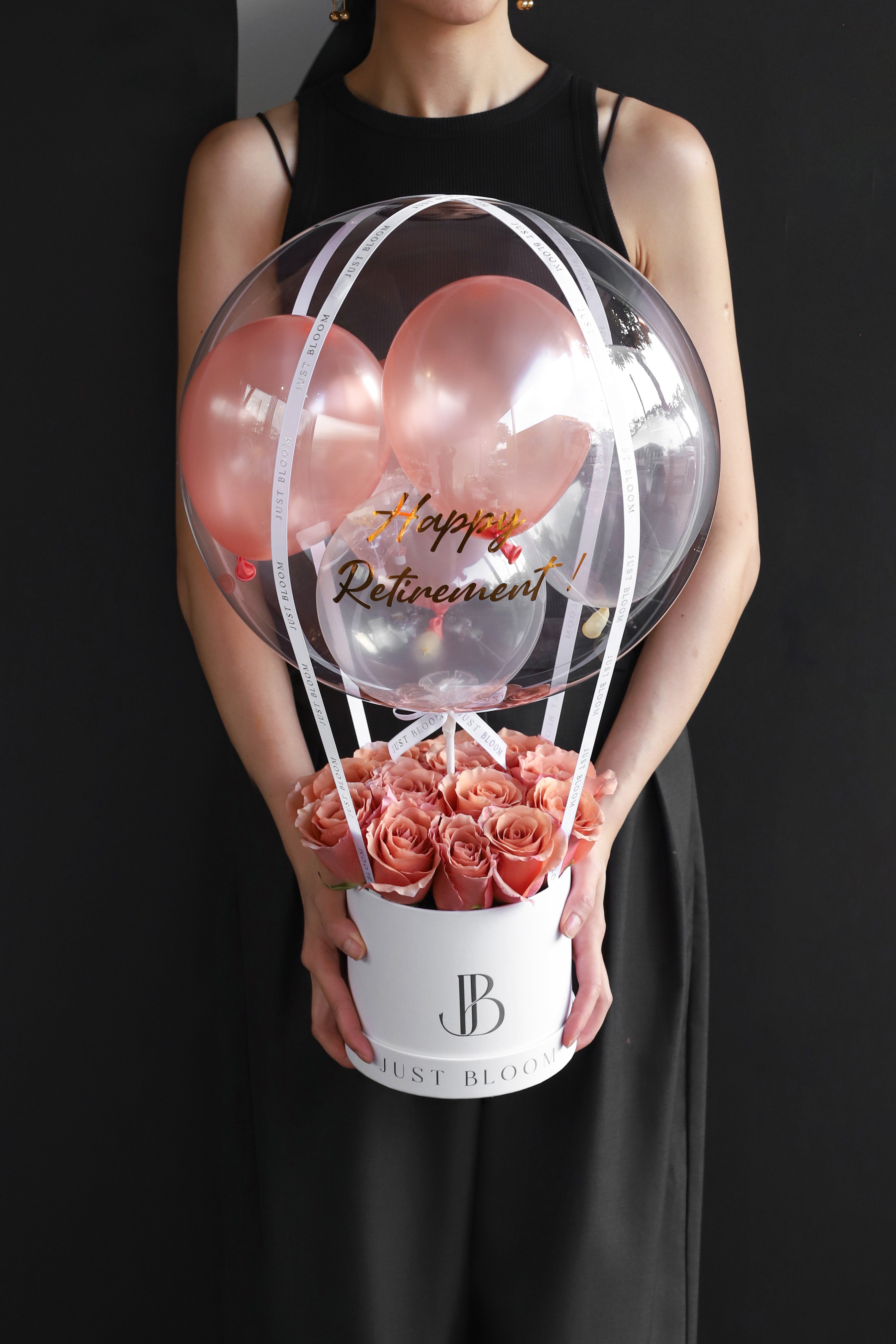 Model holding an all-blush and salmon rose balloon flower box with a large crystal balloon containing rose-toned balloons in a white Just Bloom round box against a dark background — Just Bloom Hong Kong