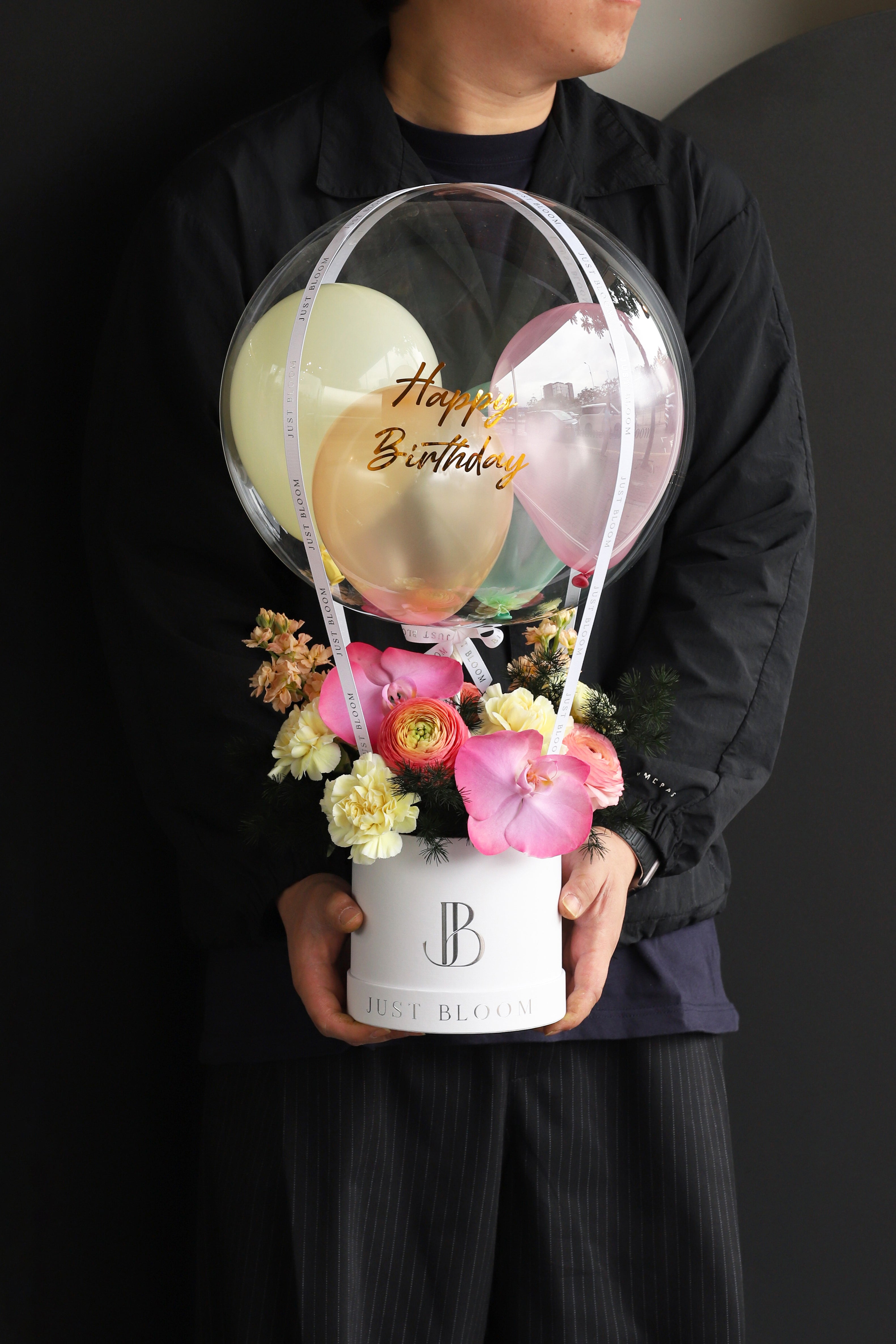 Model holding a fresh flower box with pink Phalaenopsis Orchids, Ranunculus, and Carnations in a white Just Bloom round box against a dark background — Just Bloom Hong Kong