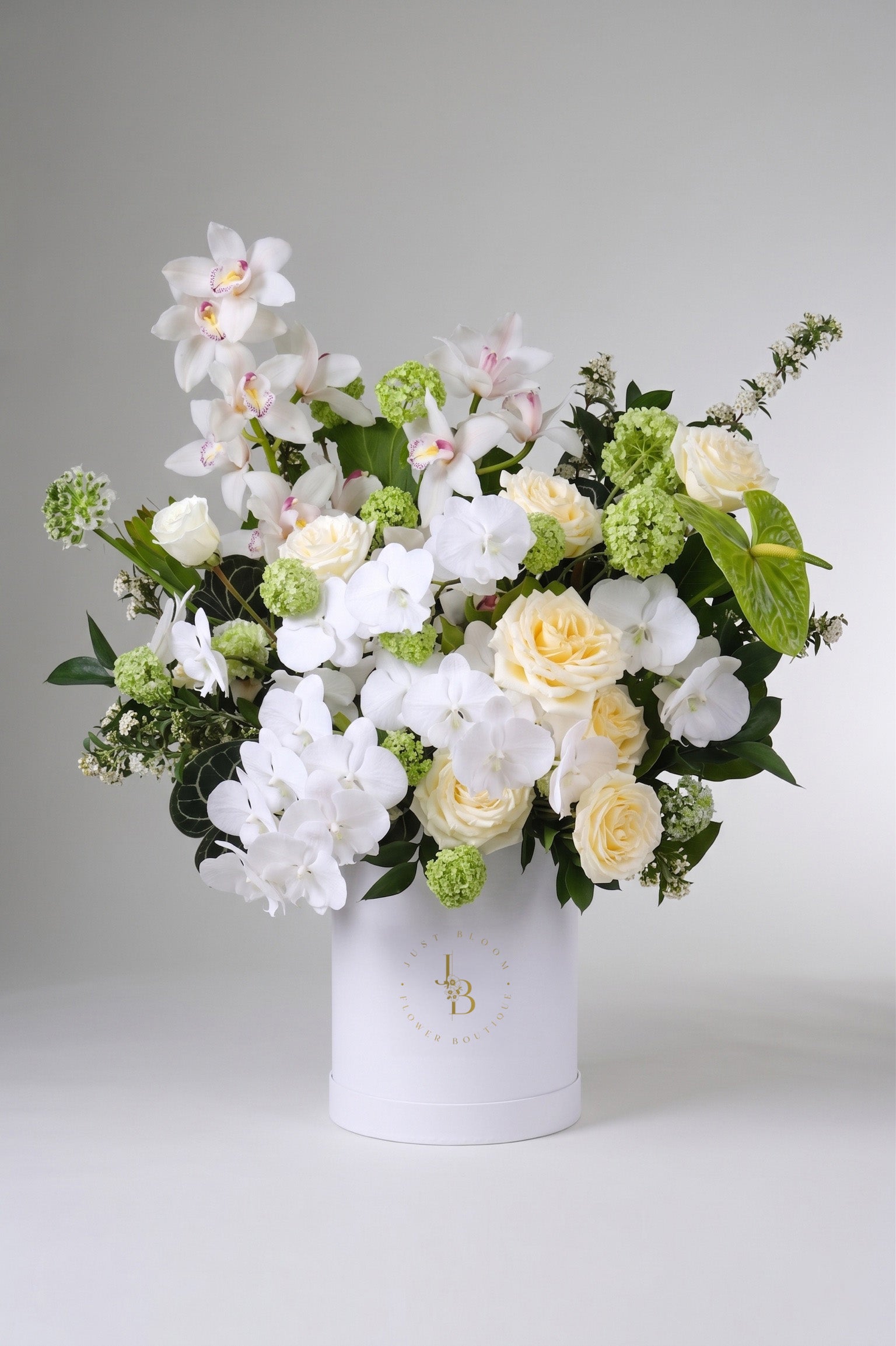  A luxury white flower box by Just Bloom Hong Kong featuring white phalaenopsis orchids, cymbidium orchids, cream roses, green viburnum and anthuriums arranged in a signature white Just Bloom hat box