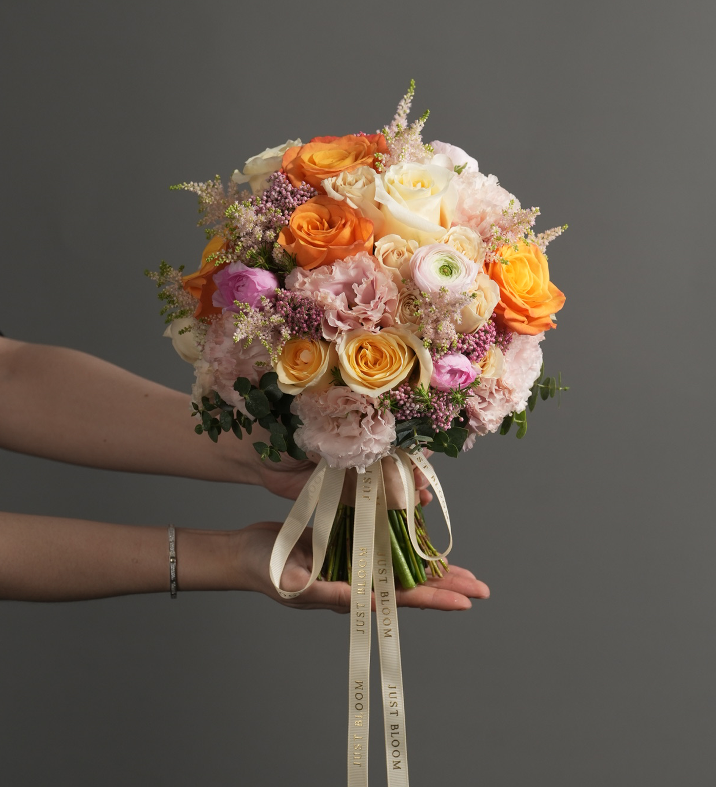 Colorful flower arrangement in a glass vase featuring orange Ecuadorian roses, Canterbury bells, giant alliums, and spring pastels beside books.