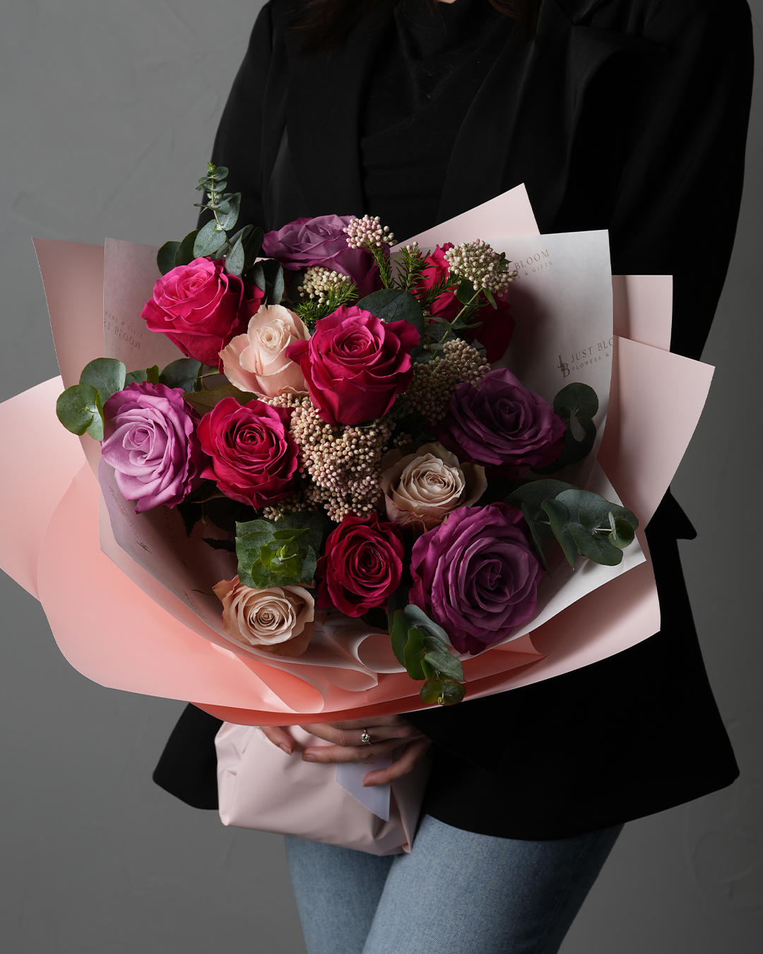 Emmalynn bouquet with purple and magenta roses wrapped in soft pink, held in front of a black outfit