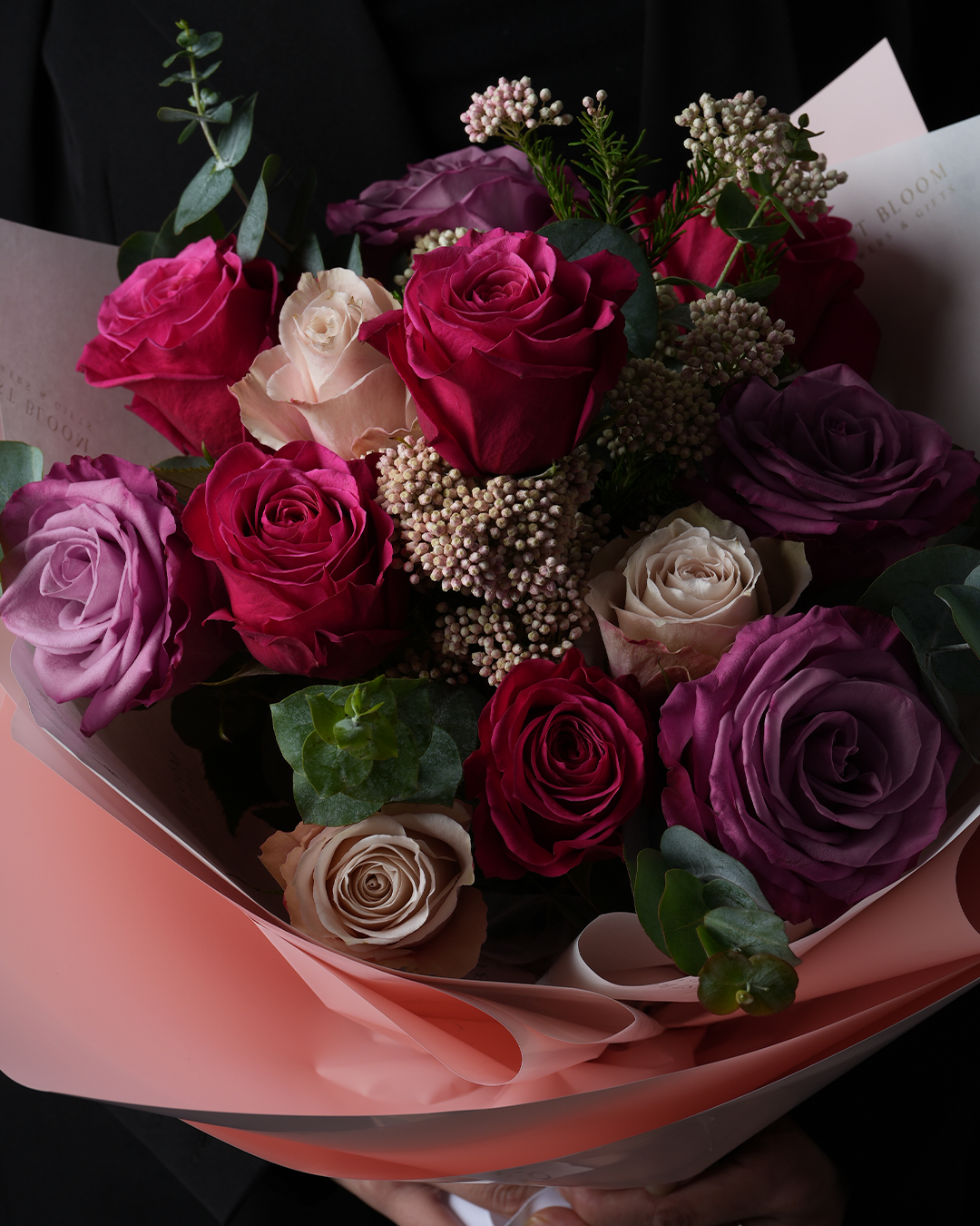 Close-up view of Emmalynn bouquet showing roses in pink, nude, and purple tones with rice flowers