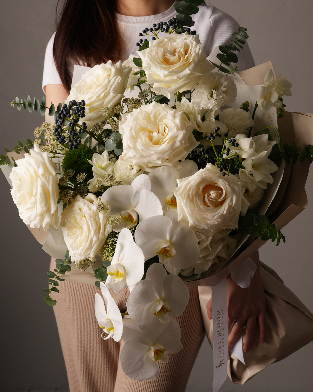 Just Bloom Genevieve bouquet with premium white garden roses, moth orchids, and seasonal fillers – held by model in studio setting, Hong Kong floral design