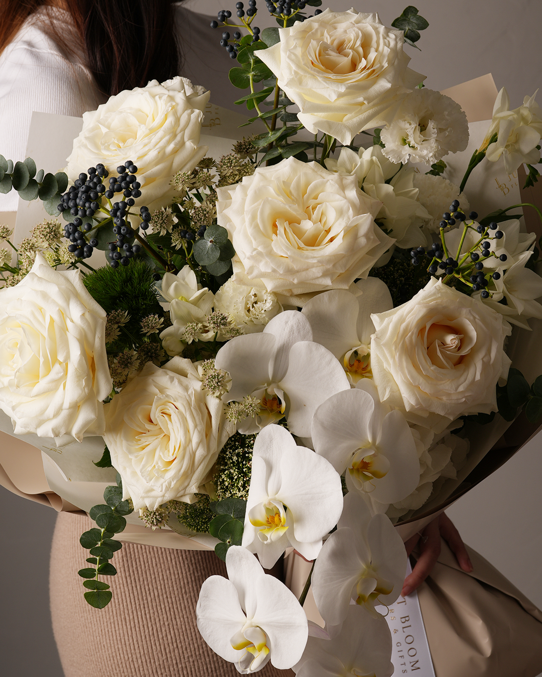 ust Bloom Genevieve floral bouquet in white tones, showcasing orchids, garden roses, and dark berries – styled side angle for modern gifting in Hong Kong