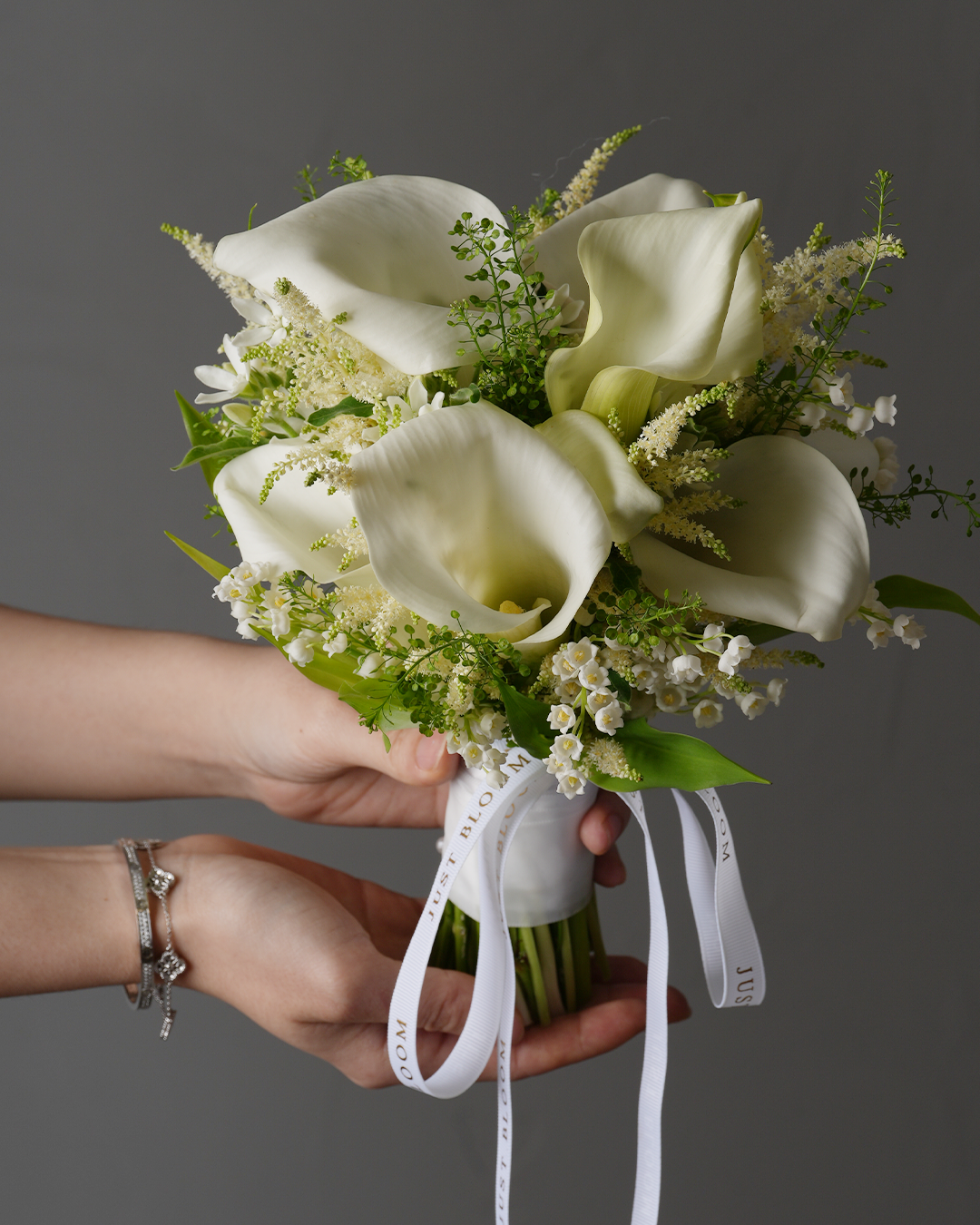 Just Bloom Finley bridal bouquet with white calla lilies and lily of the valley held in hands
