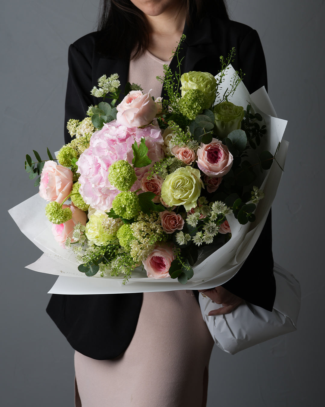 Leilani pink hydrangea and green rose mixed bouquet held by woman in black blazer with white wrapping