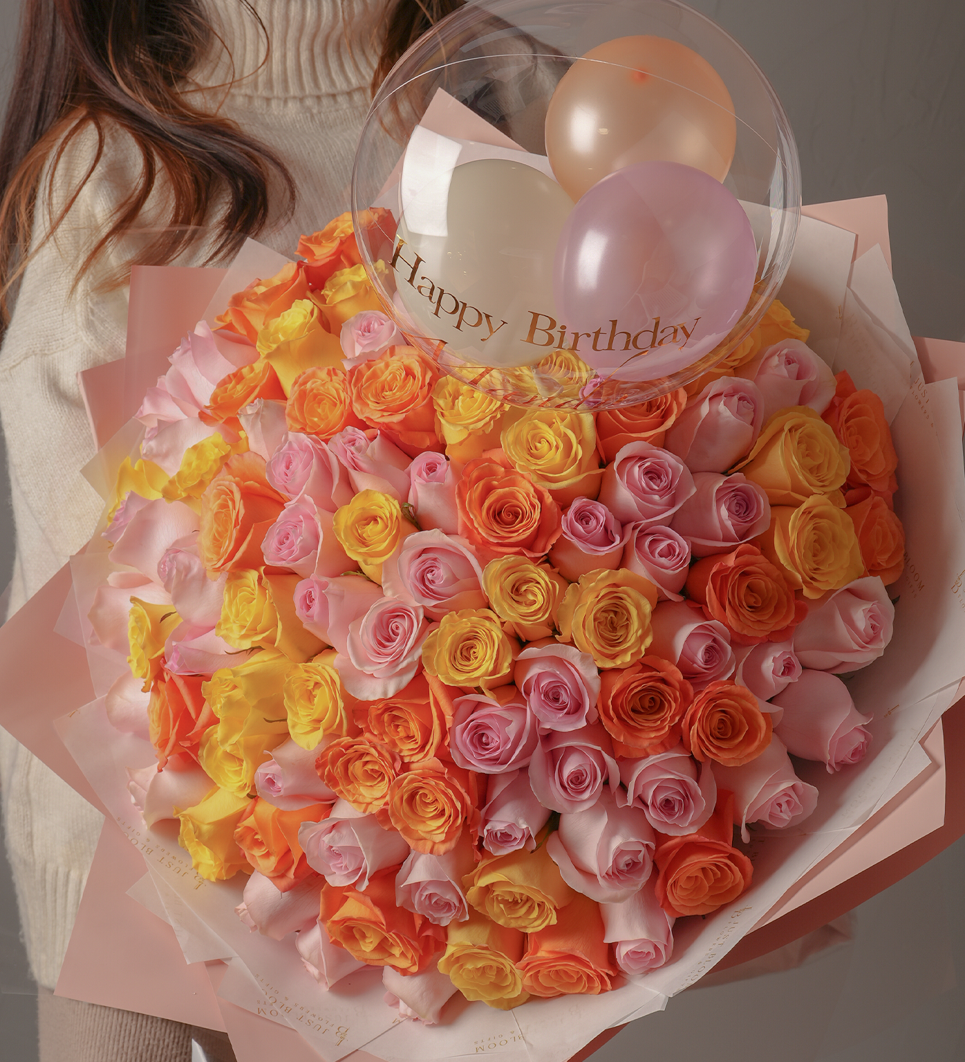Close-up of colorful 99-stem rose bouquet in pink, yellow, and orange shades with pastel wrapping