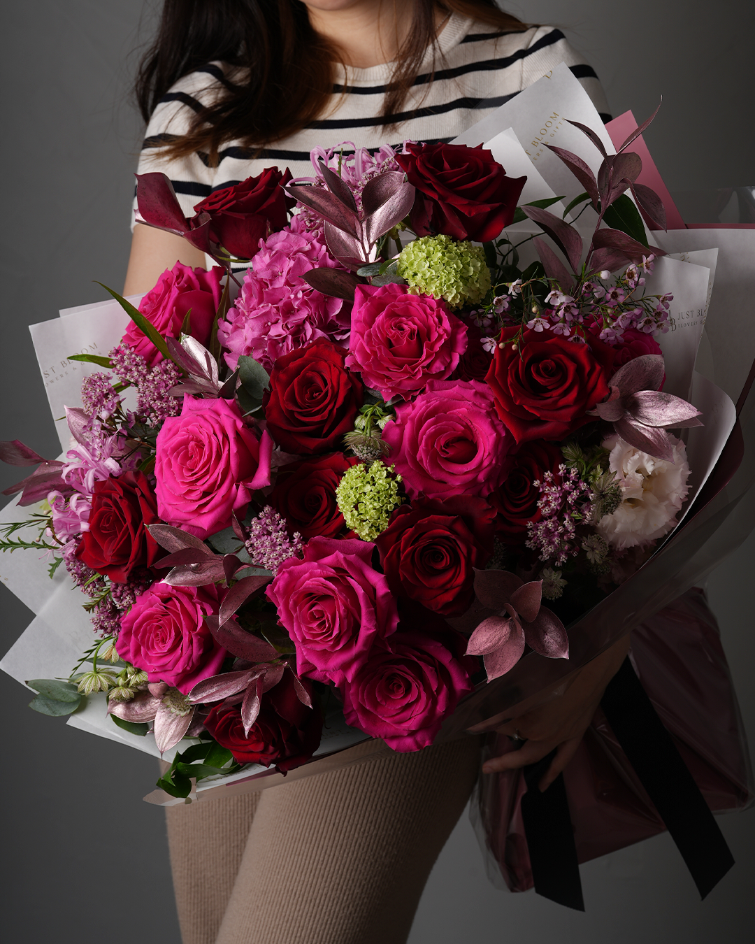 Lucia dramatic red and pink large rose bouquet held by woman in striped top with elegant wrapping