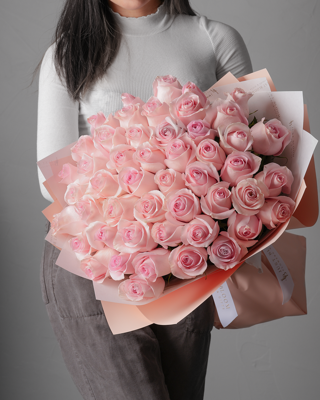Person in white turtleneck holding Marley bouquet with soft pink roses wrapped in blush paper