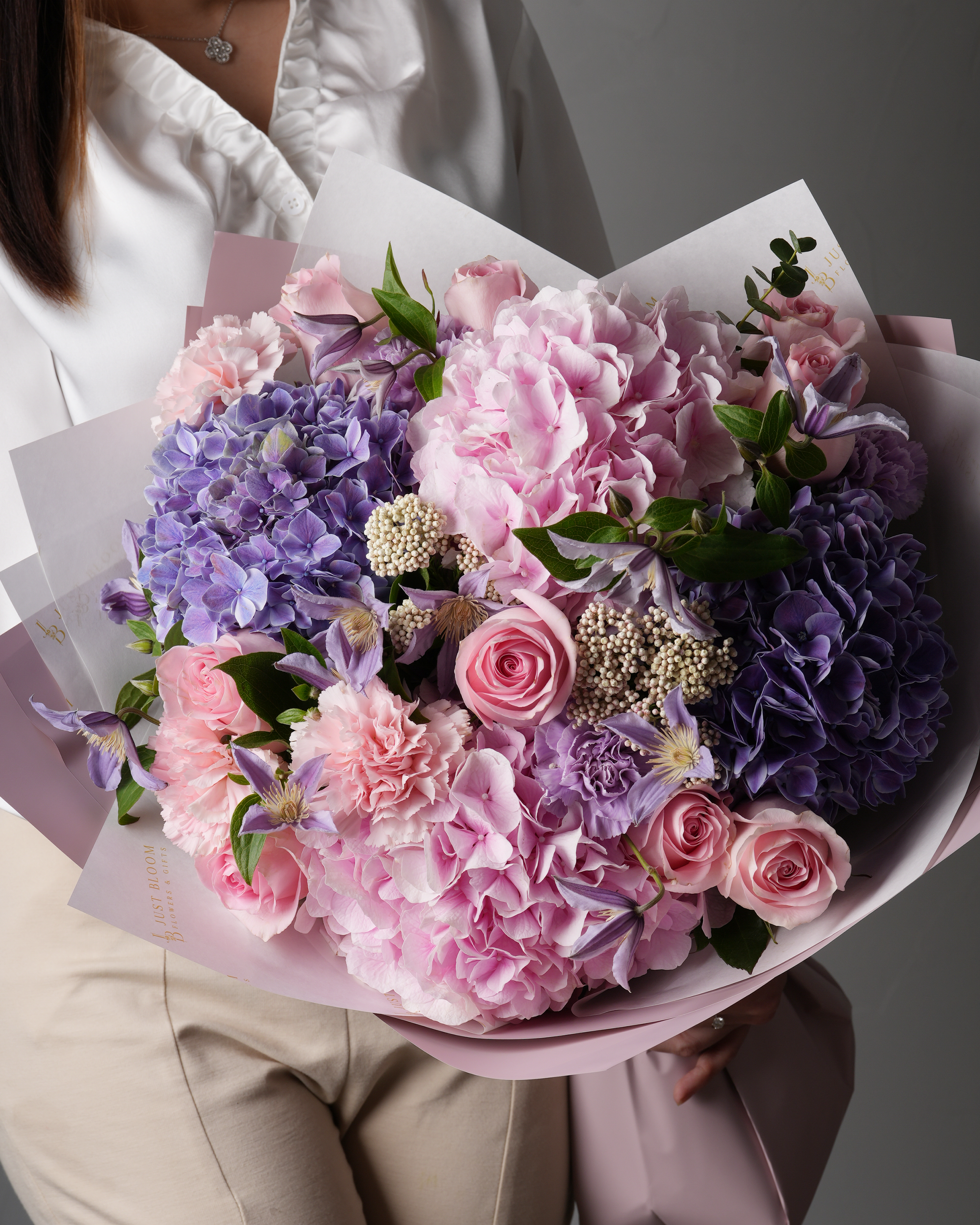 Close-up view of a luxurious flower bouquet featuring pink hydrangeas, purple clematis, roses, carnations, and delicate rice flowers.