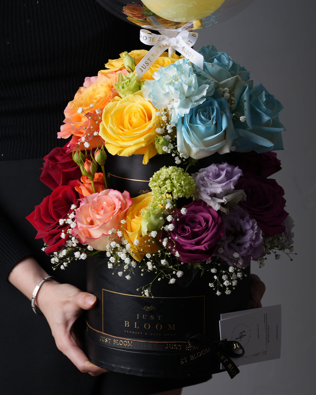 Rainbow Cake floral arrangement featuring red, yellow, blue, purple roses and crystal balloon in black hatbox