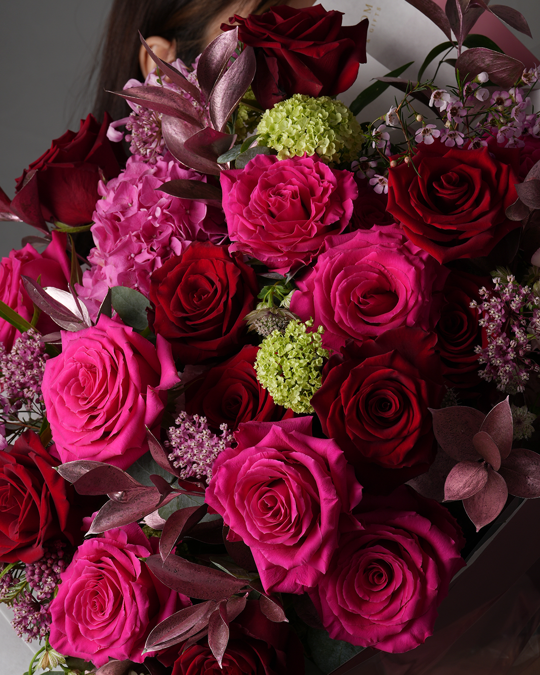 Close-up view of Lucia bouquet showing deep red roses, pink roses, and purple foliage arrangement